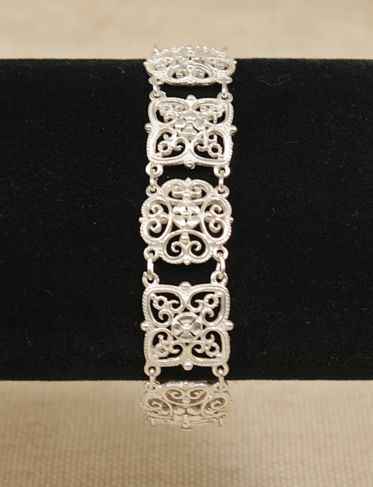 Edwardian silver gothic revival design filigree bracelet on a black stand with a beige background