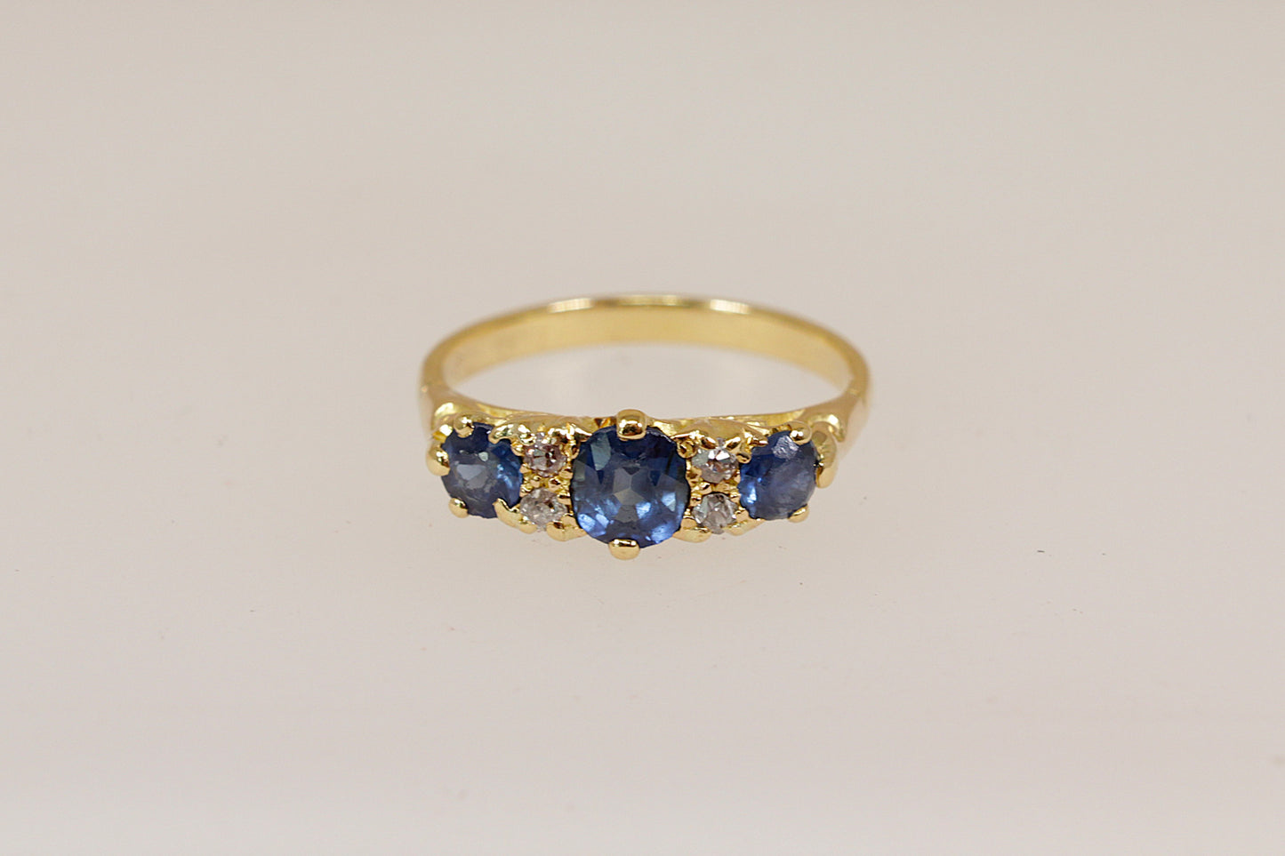 Gold ring with blue sapphire and diamond gemstones on a beige background