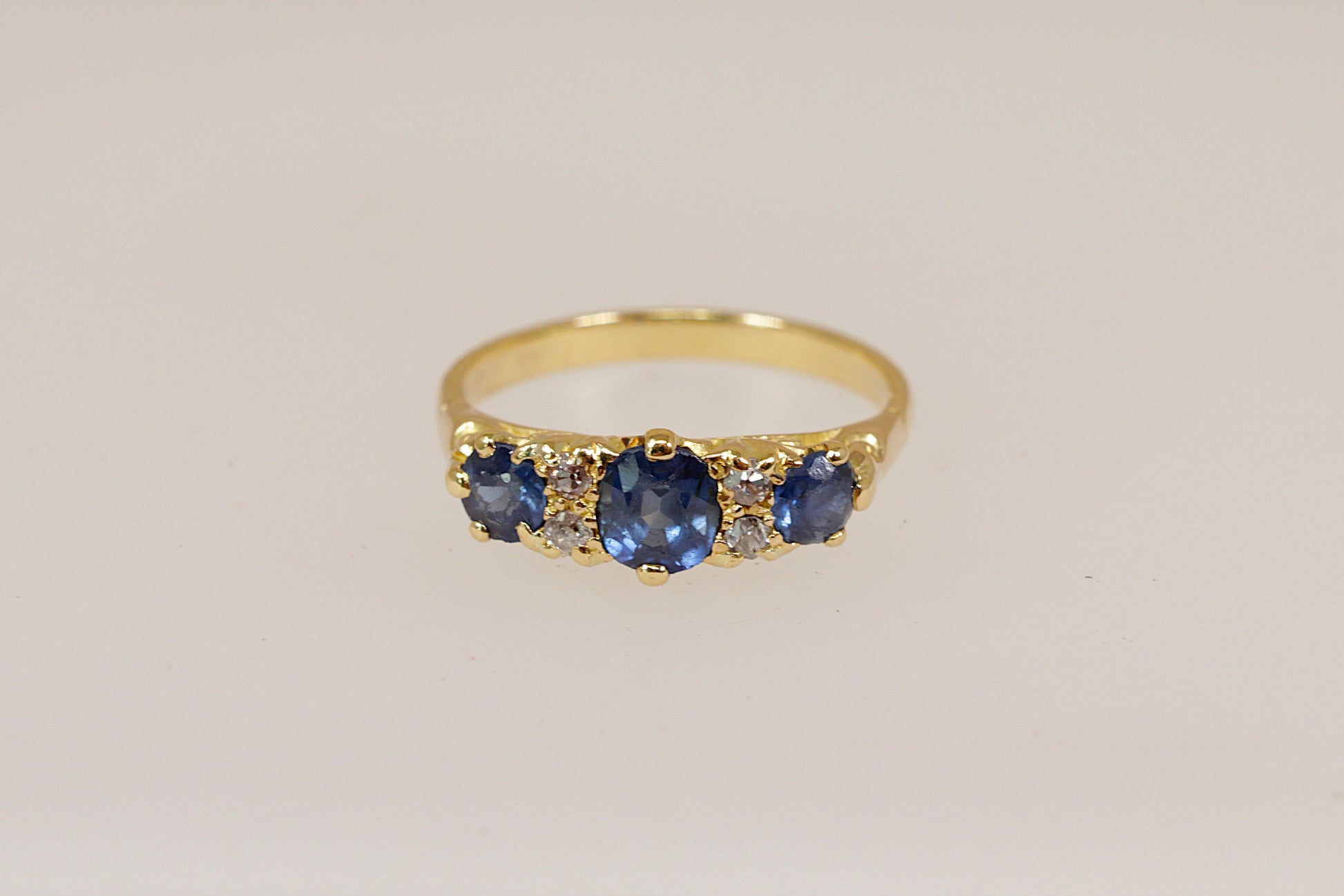 Gold ring with blue sapphire and diamond gemstones on a beige background