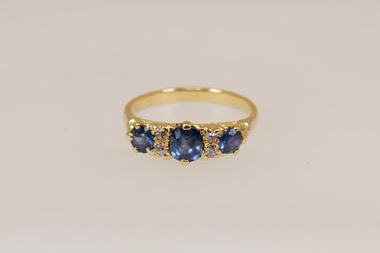 Gold ring with blue sapphire and diamond gemstones on a beige background