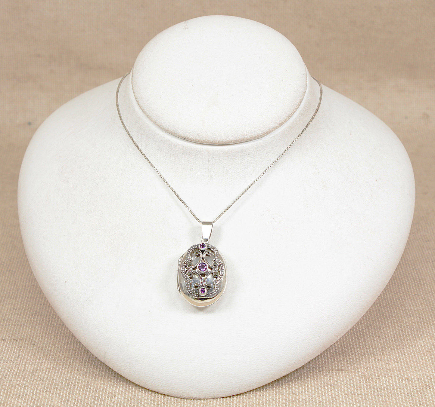 Vintage silver pendant locket necklace  with amethyst gemstones on a white bust against a beige background
