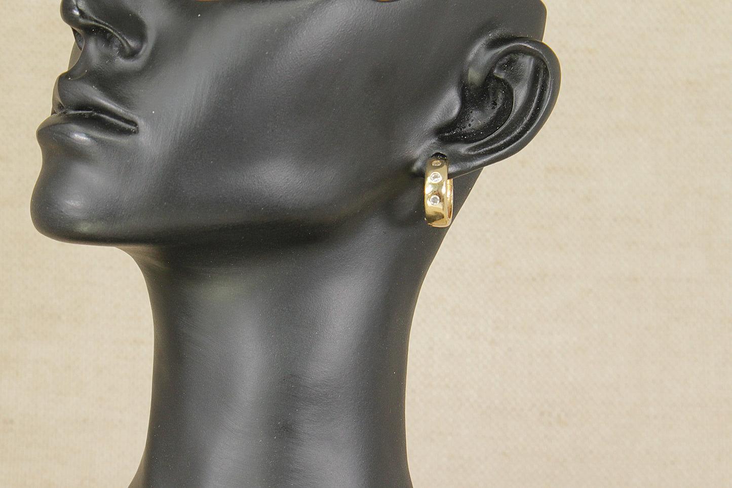 Gold hoop earring on a black mannequin head against a beige background