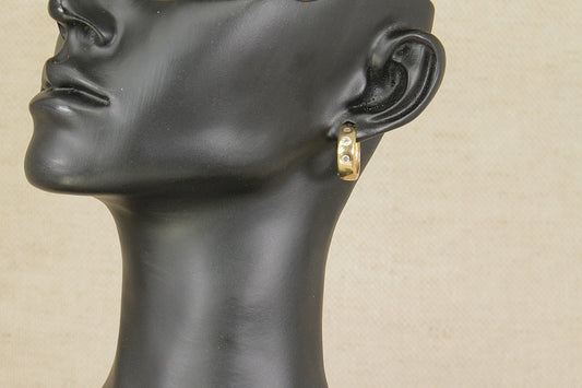 Gold hoop earring on a black mannequin head against a beige background