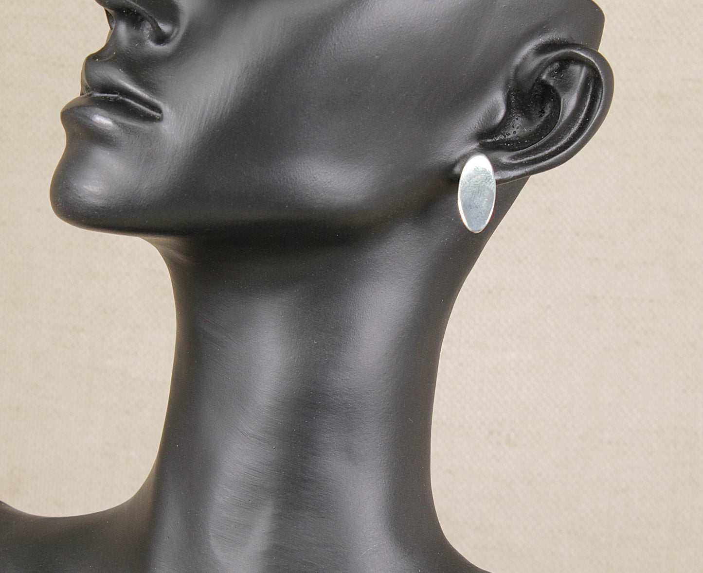 Mannequin head with a silver earring on a beige background