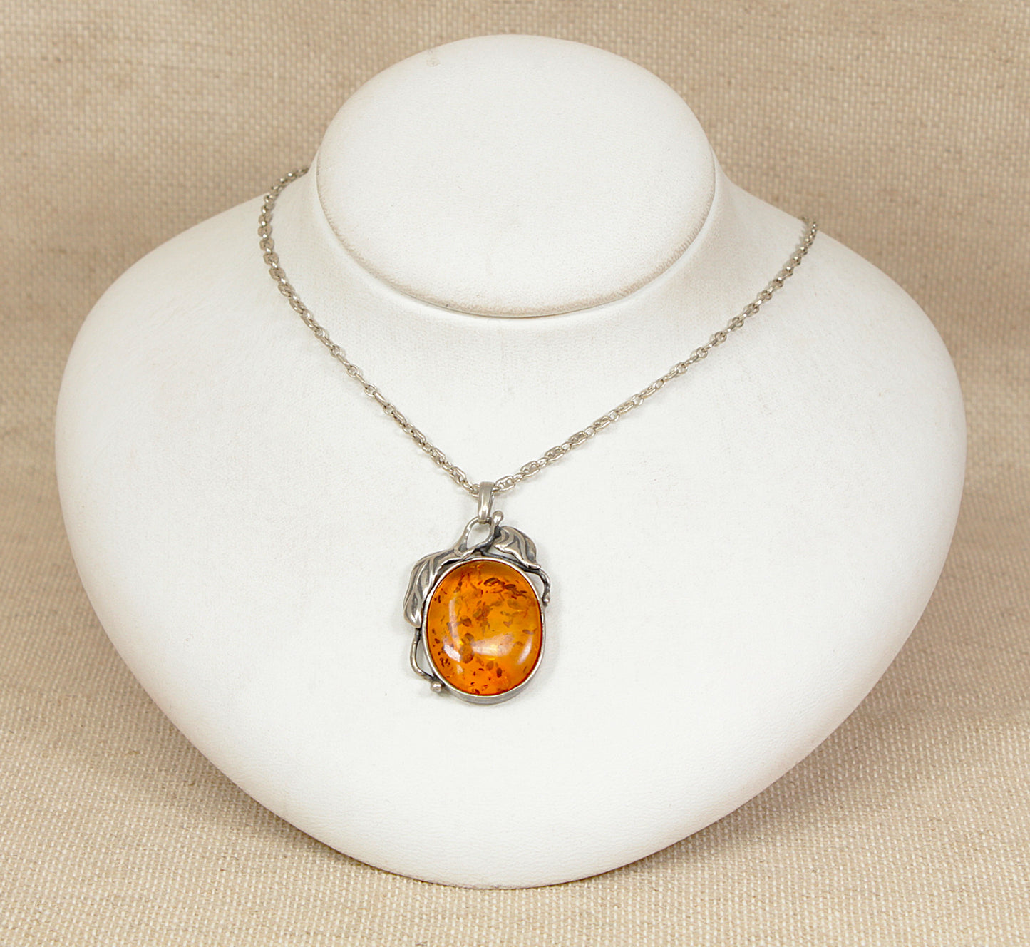 Silver necklace with an amber pendant on a white stand against a beige background