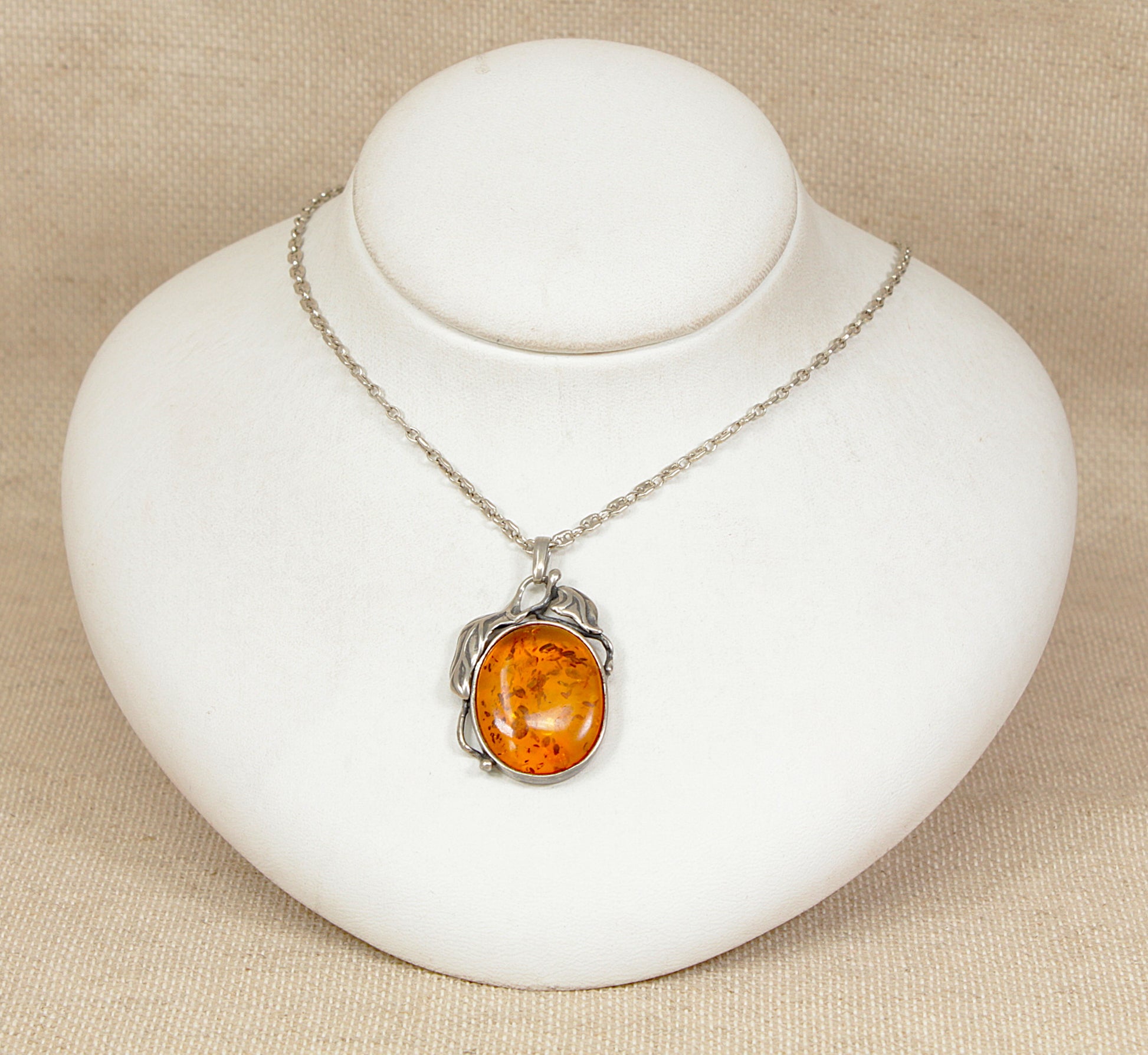 Silver necklace with an amber pendant on a white stand against a beige background