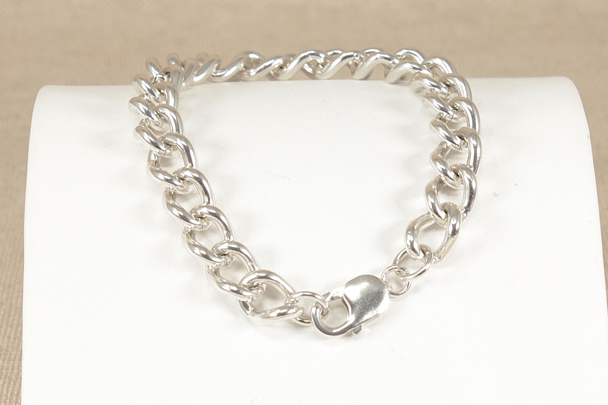Silver chain bracelet on a white cushion with a beige background