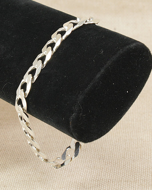 Silver flat curb link chain bracelet on a black velvet stand with a beige background