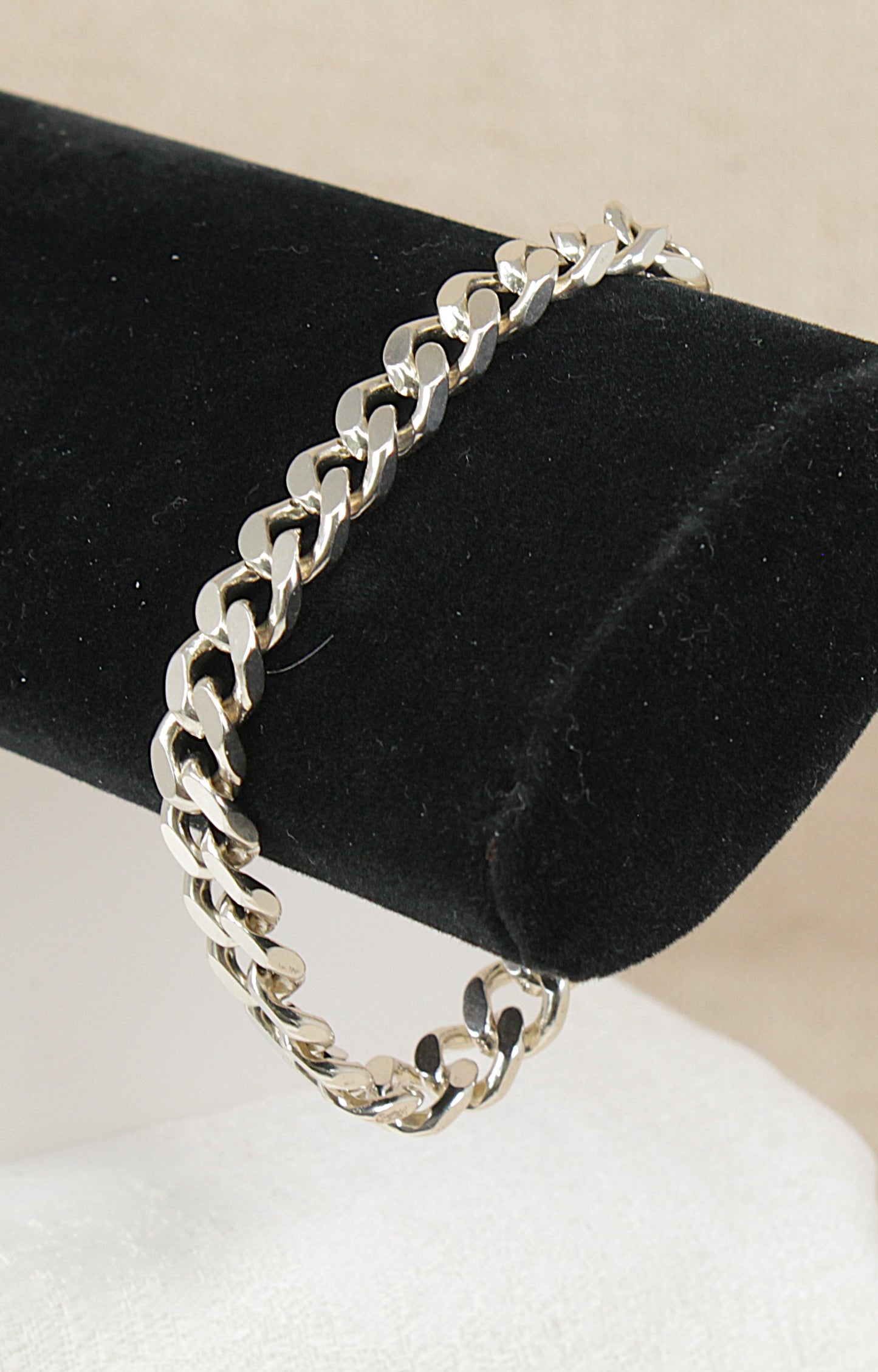 Silver flat curb link chain bracelet on a black velvet stand with a beige background