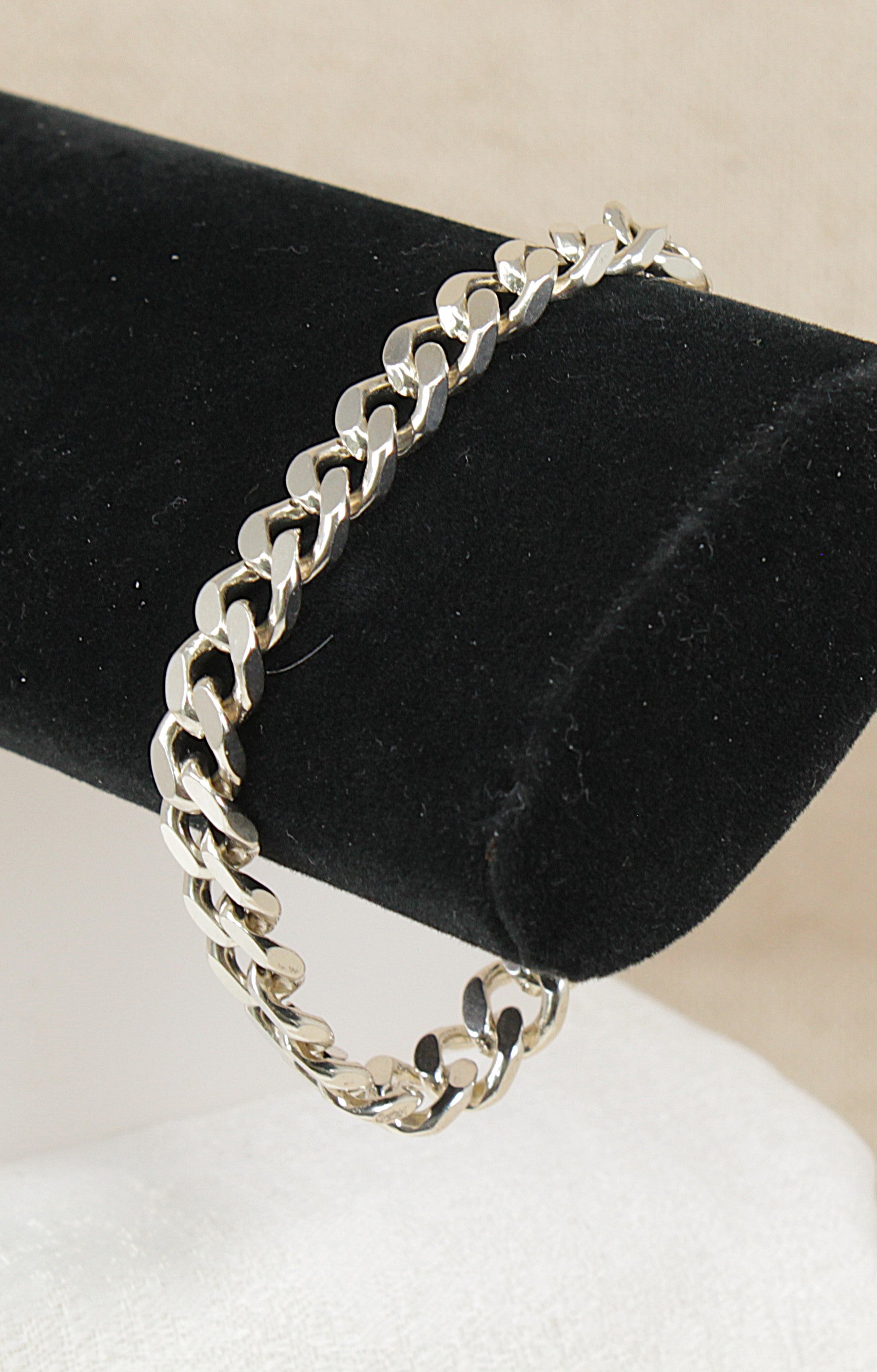 Silver flat curb link chain bracelet on a black velvet stand with a beige background