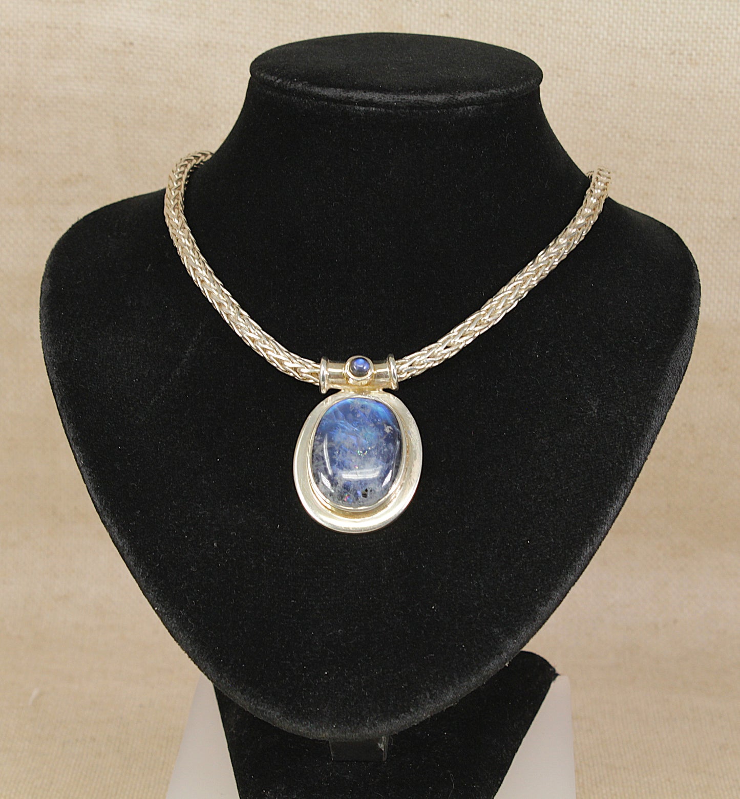 Statement Necklace with a blue flash labradorite pendant on a black velvet stand against a beige background