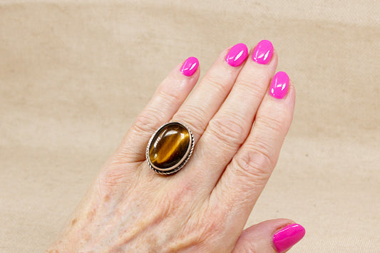 Hand wearing a statement ring with a large brown tiger's eye gemstone on a beige background