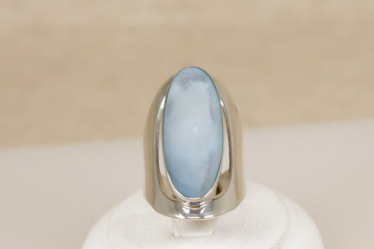Silver ring with a large oval mother of pearl gemstone on a beige background