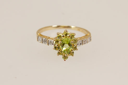 A vibrant and eye-catching 9ct gold ring, featuring a beautifully cut pear-shaped peridot at its centre. Surrounding the main stone is a sparkling halo of 10 smaller peridots, all claw set in an elegant basket setting that enhances the ring’s depth and brilliance. The stepped shoulders are adorned with delicate diamond accents, adding a refined sparkle and completing the luxurious design. Inside the band, the ring is clearly stamped 375 and 9K, confirming its gold purity. UK Finger size: N ½.