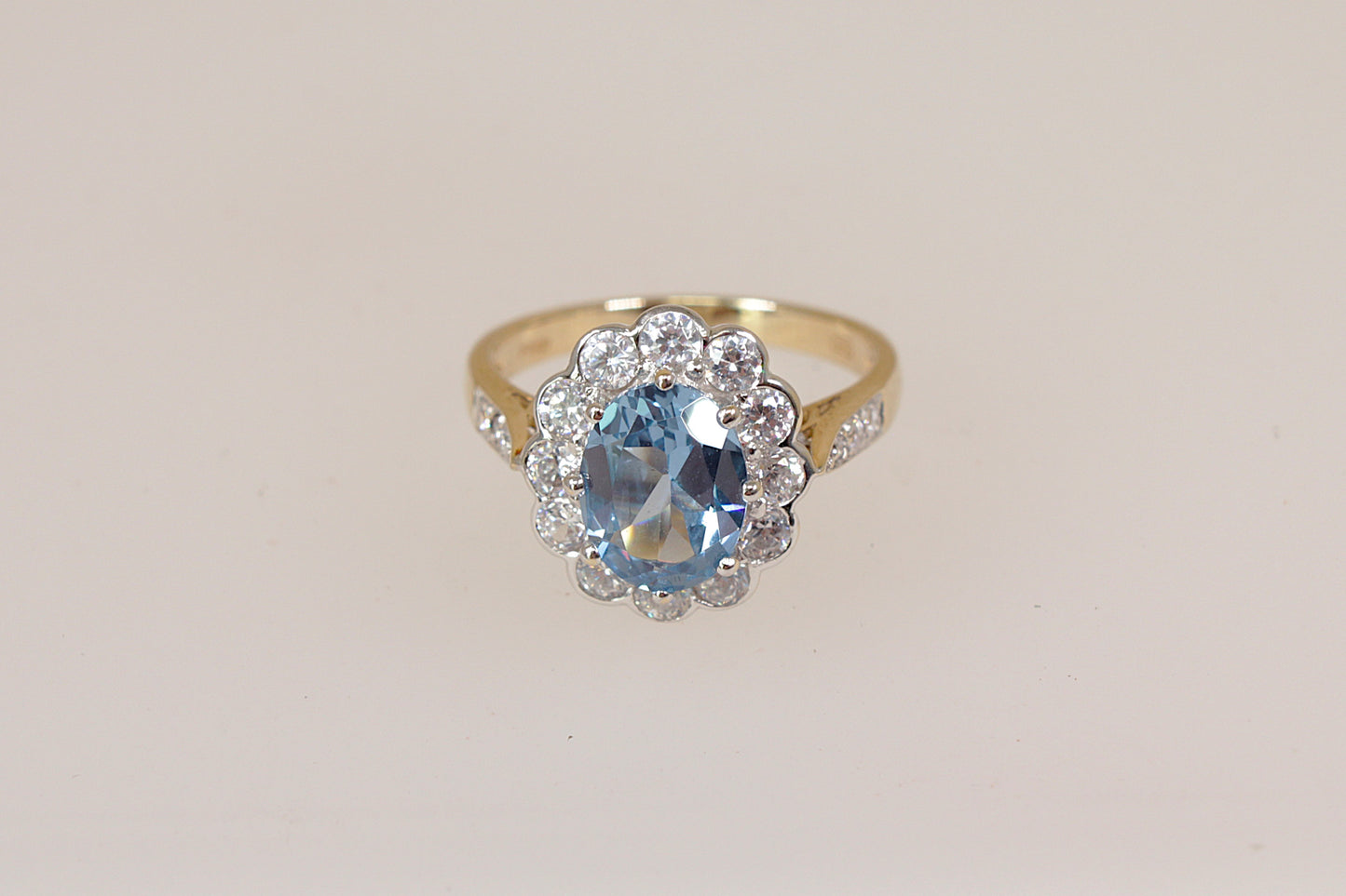 Gold ring with a blue topaz gemstone and cz diamond simulant gemstone accents on a light beige background