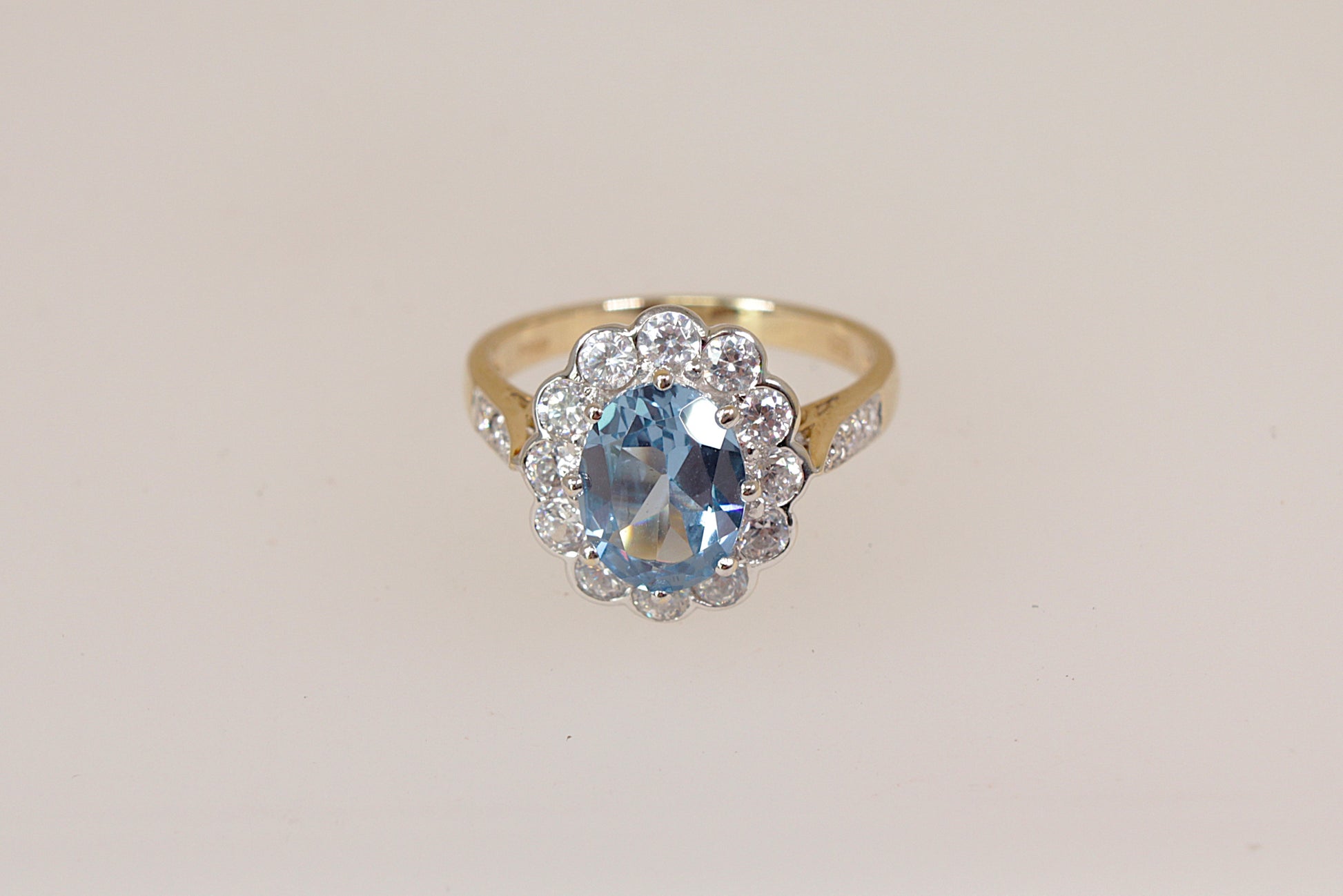 Gold ring with a blue topaz gemstone and cz diamond simulant gemstone accents on a light beige background