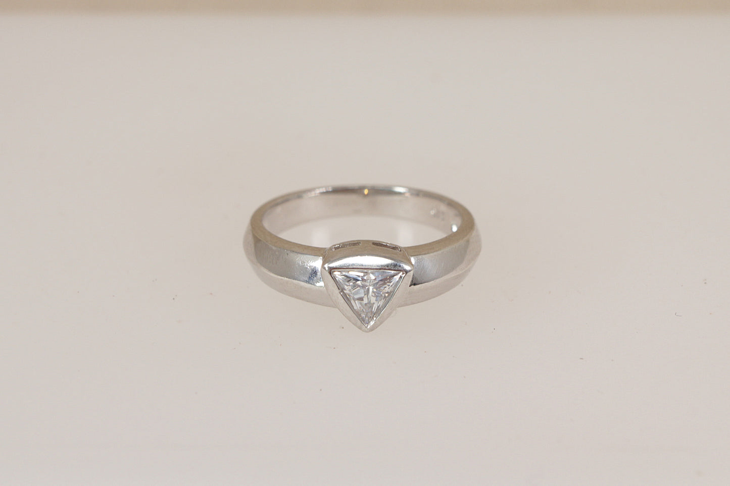 Silver ring with a triangular diamond simulant cz cubic zirconia gemstone on a light beige background