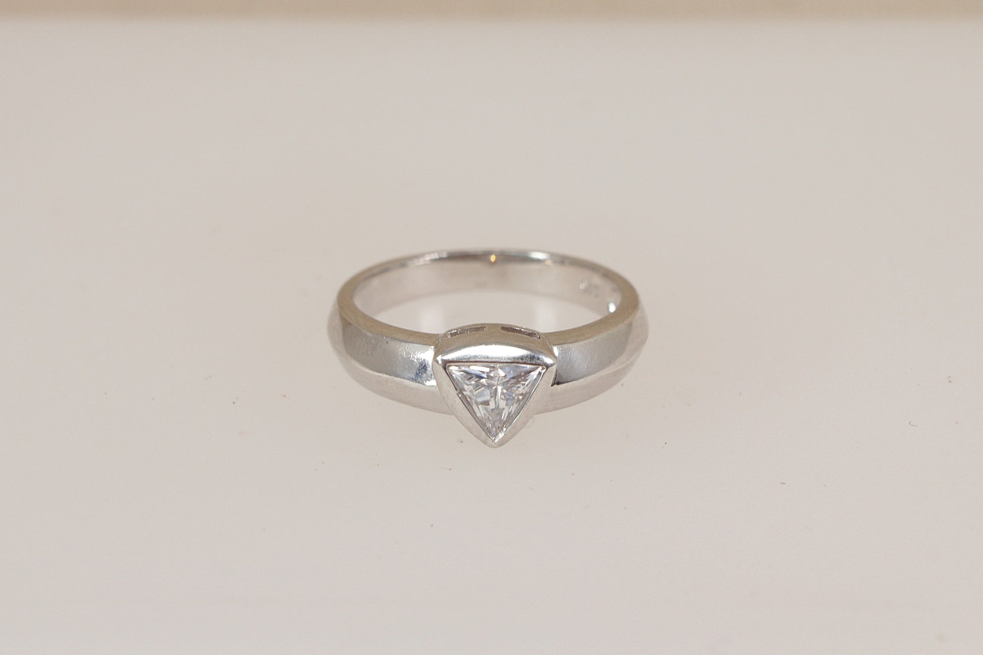 Silver ring with a triangular diamond simulant cz cubic zirconia gemstone on a light beige background