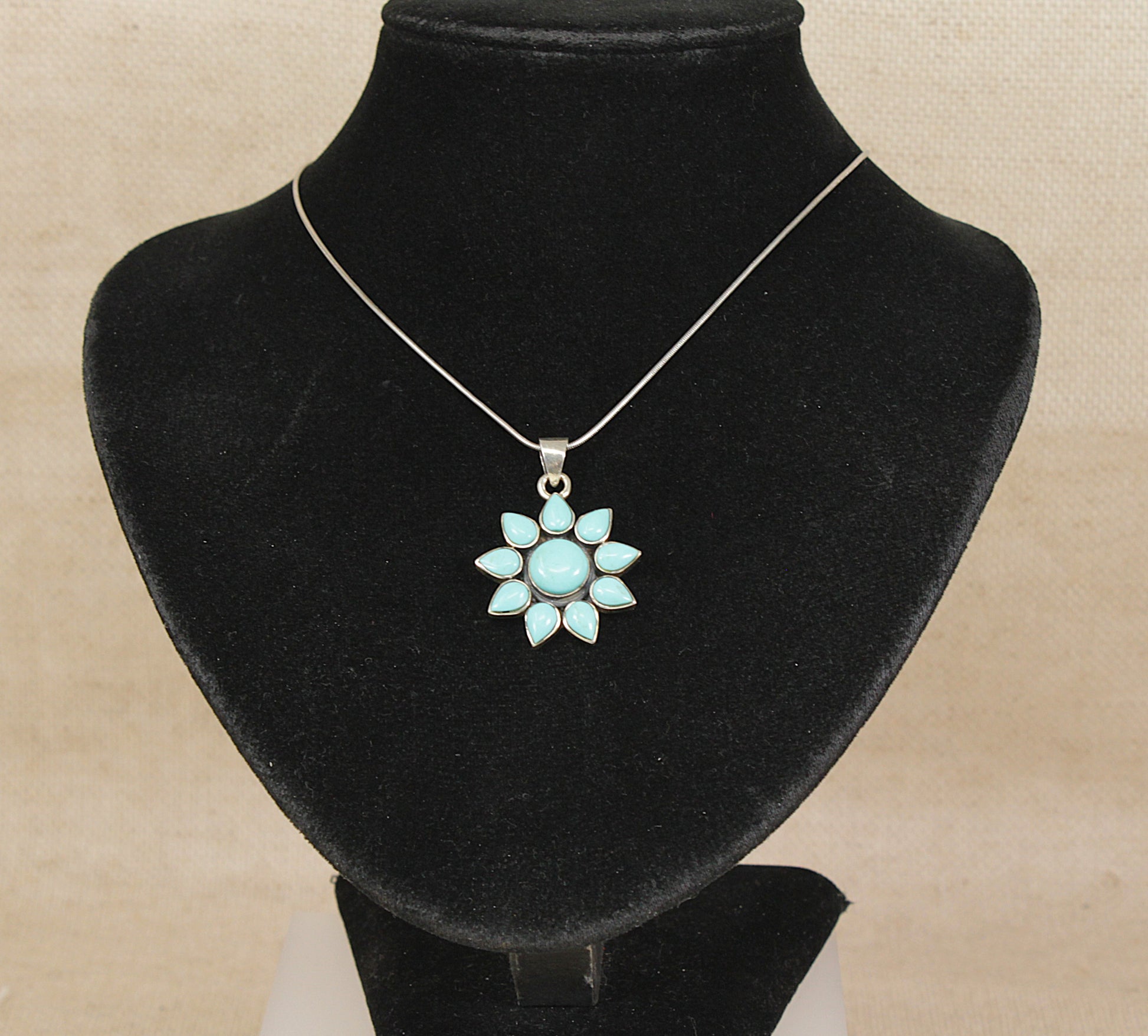 Turquoise flower pendant necklace on a black velvet stand with a beige background