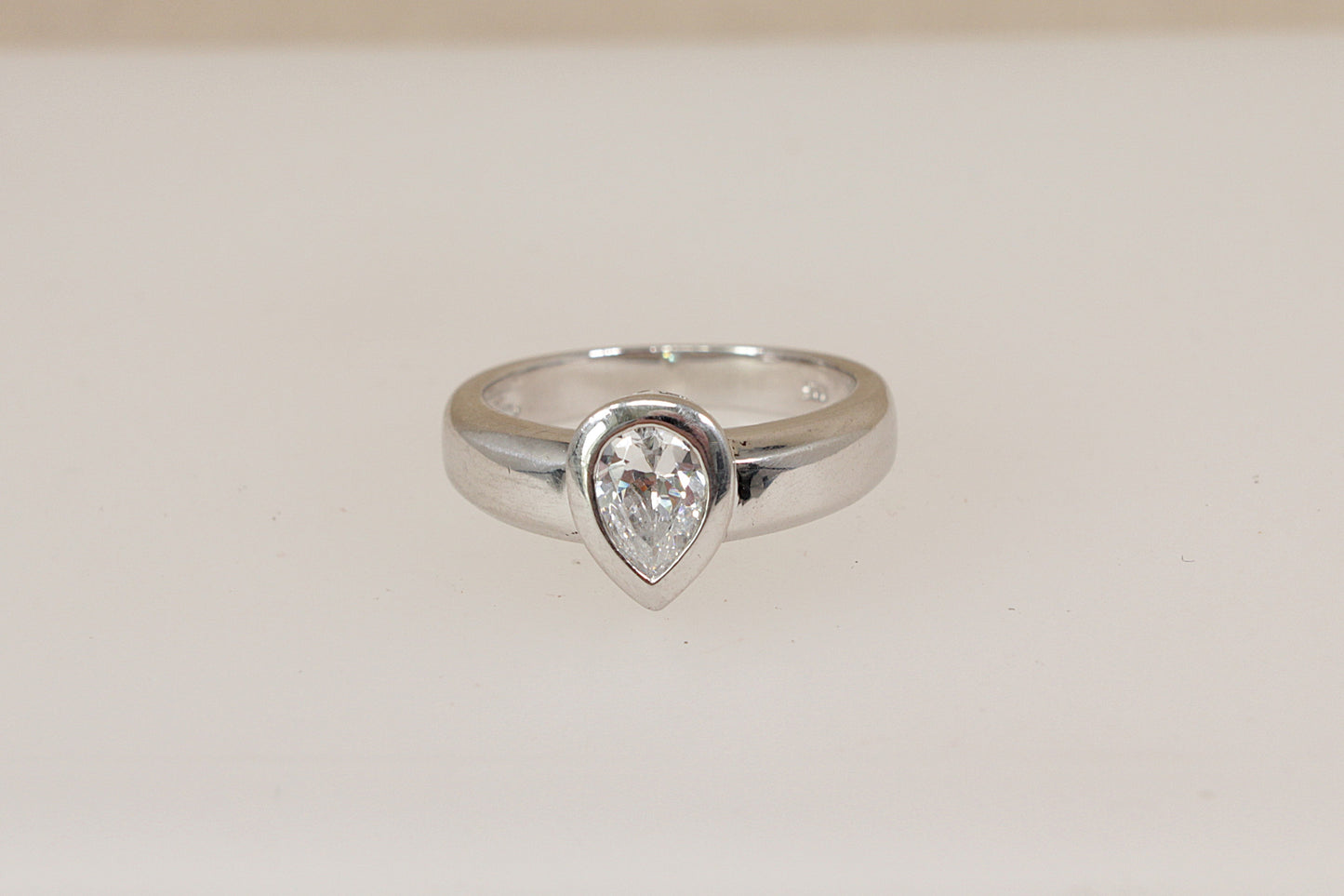 Silver ring with a teardrop-shaped cz cubic zirconia (diamond simulant) gemstone on a light beige background