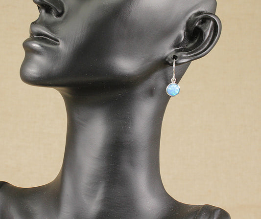 Mannequin head wearing a silver earring with a blue gemstone on a beige background