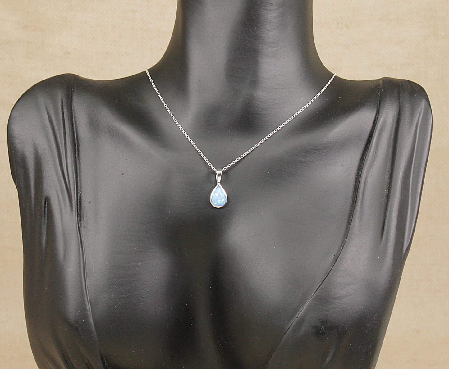 Mannequin wearing a silver necklace with a blue pendant on a beige background