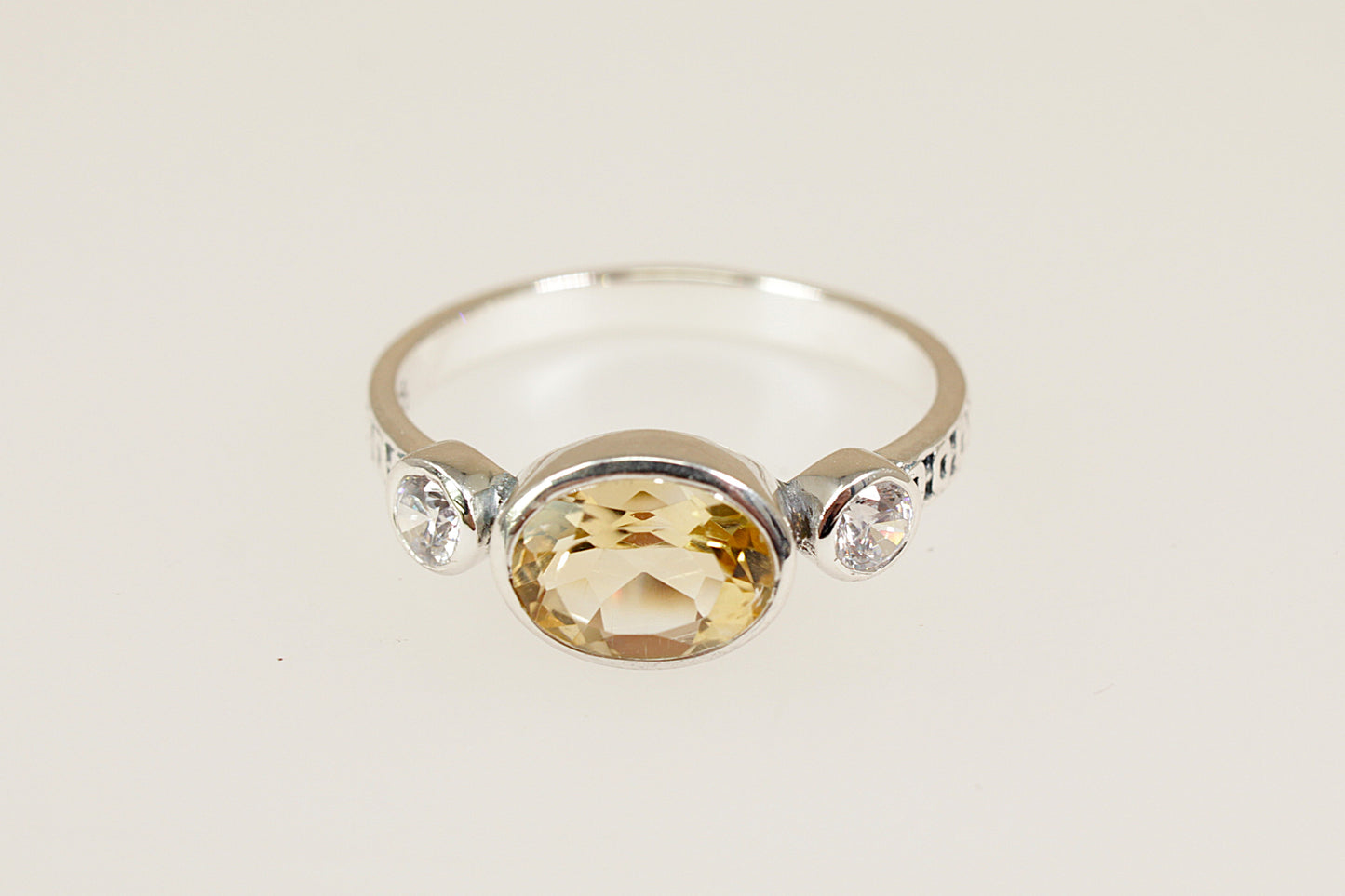 Silver ring with a yellow gemstone and smaller clear stones on a light background