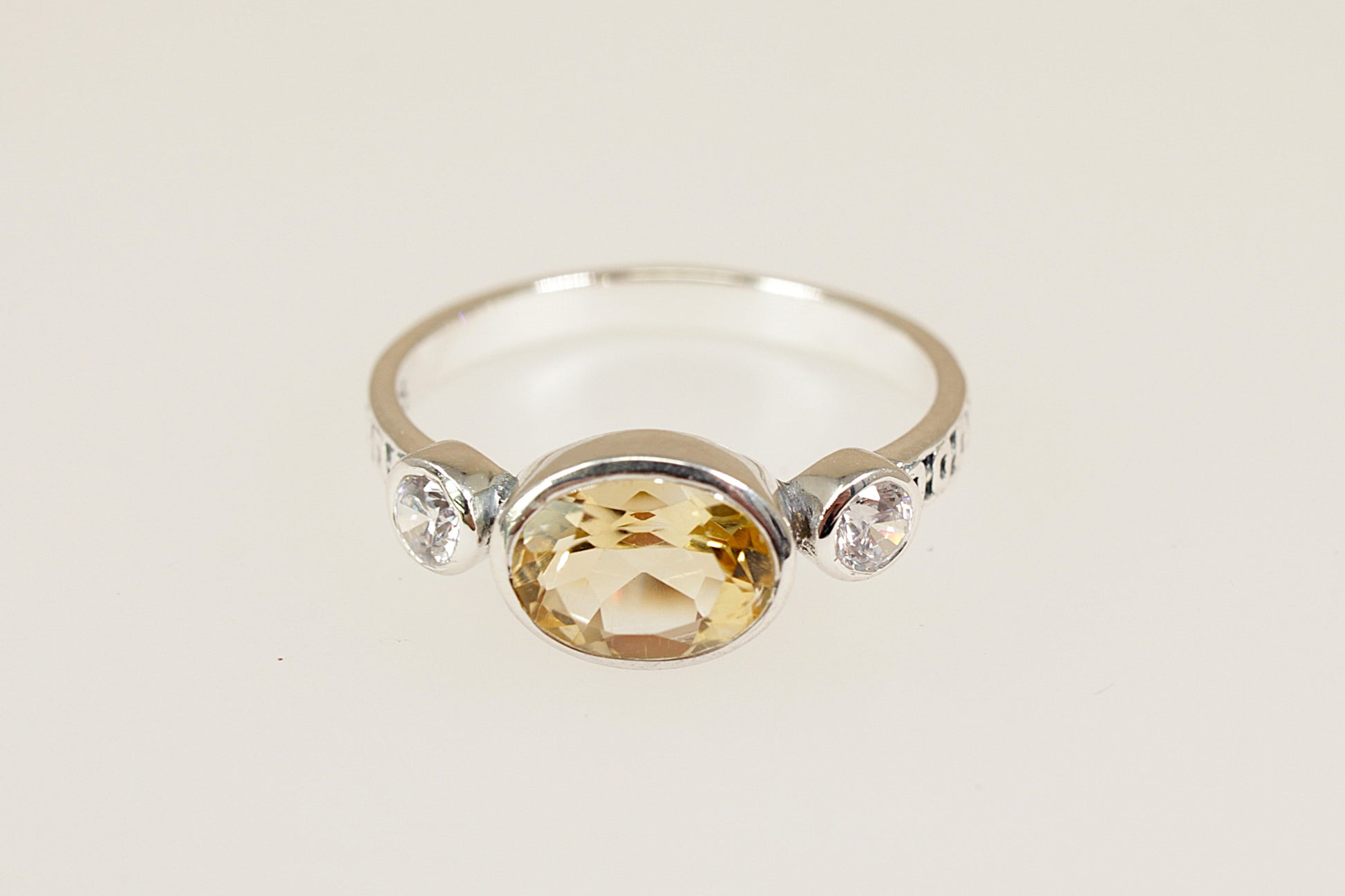 Silver ring with a yellow gemstone and smaller clear stones on a light background