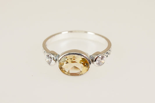 Silver ring with a yellow gemstone and smaller clear stones on a light background