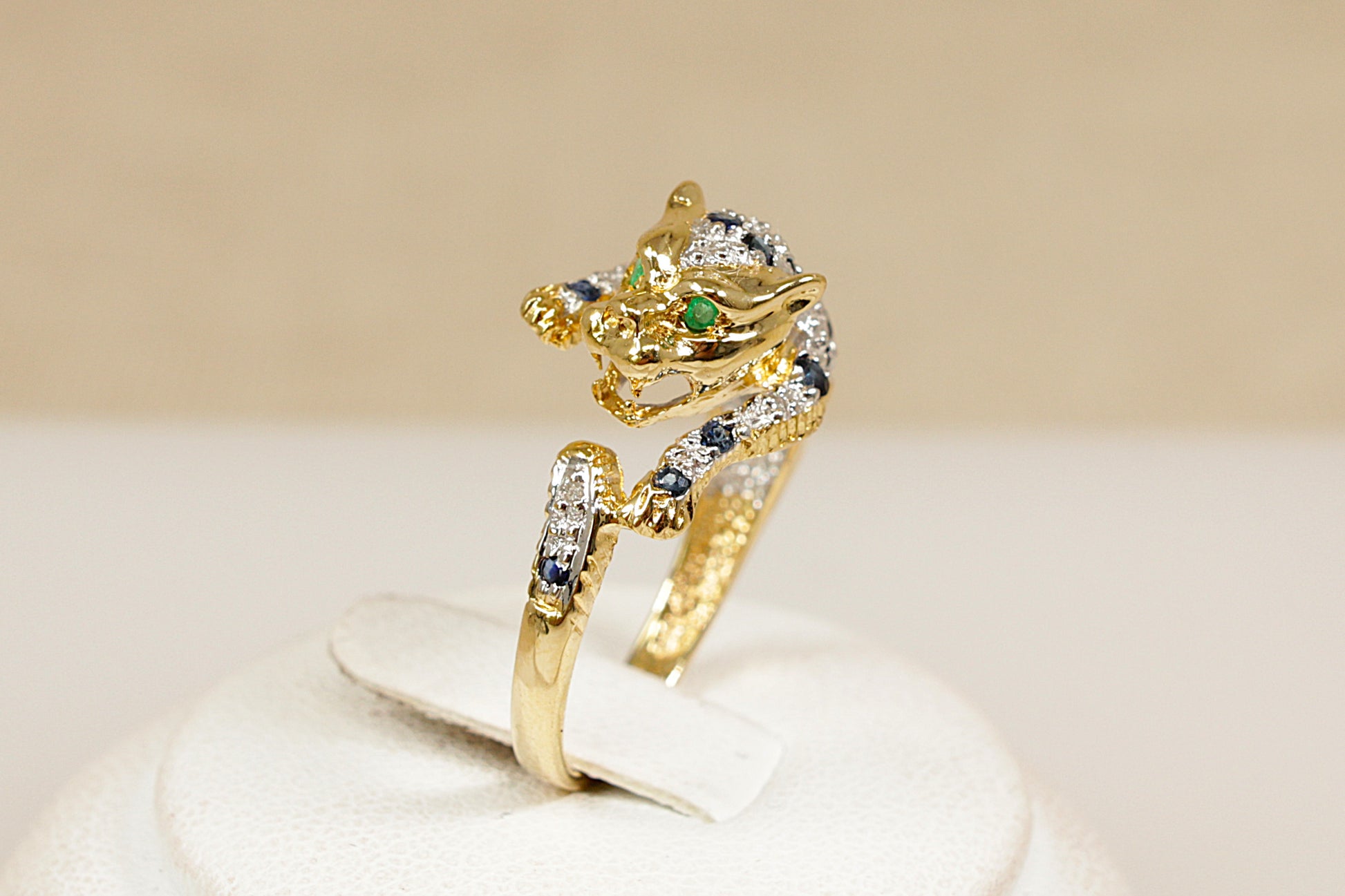 A 18ct yellow gold custom designed ring in the shape of a roaring leopard wild cat its body is encrusted with white gold, sapphires and diamonds the leopard has green emerald eyes UK finger size M.