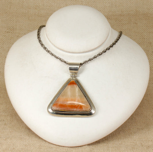 A triangular sterling silver pendant with a pinky / brown agate gemstone, mounted on a white display stand.