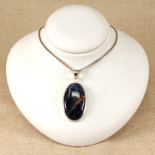 An oval-shaped agate pendant with black, purple, and copper colors, set in a silver mount, displayed on a white mannequin.