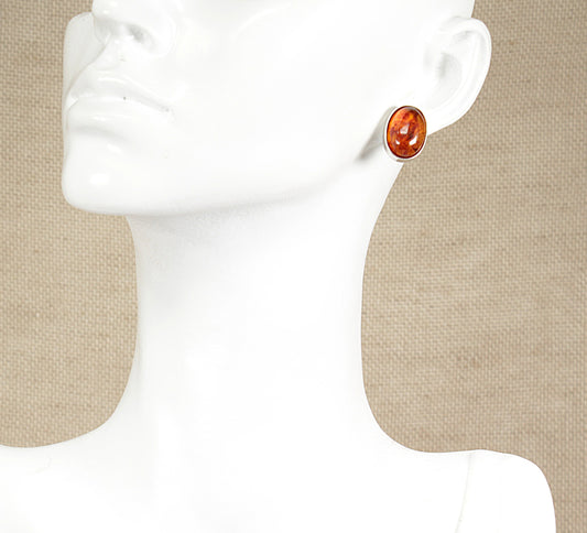 A pair of silver amber stud earrings displayed on a mannequin head.