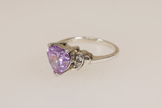 Silver ring with a heart-shaped purple amethyst colour gemstone on a light beige background
