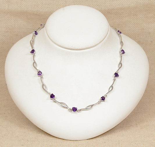Silver necklace with purple amethyst heart shape gemstones on a white stand against a beige background