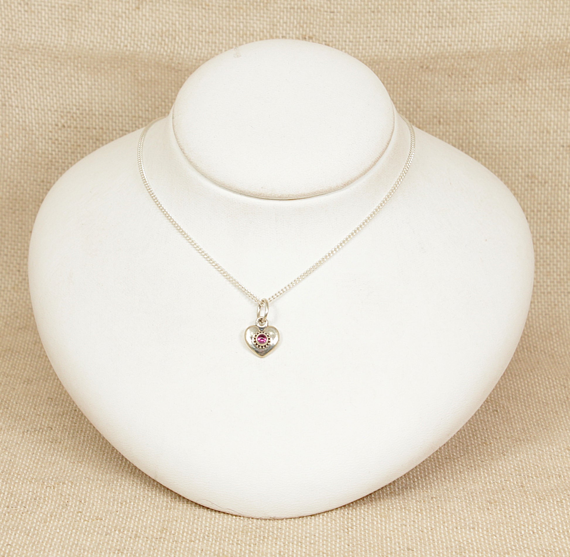 Pandora necklace with a heart-shaped pendant on a white stand against a beige background