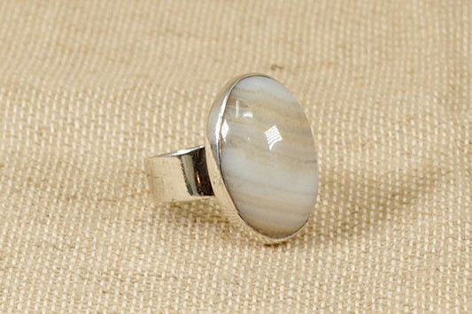 A large oval cream and brown banded agate stone set in a handcrafted solid silver ring, displayed on a textured background.
