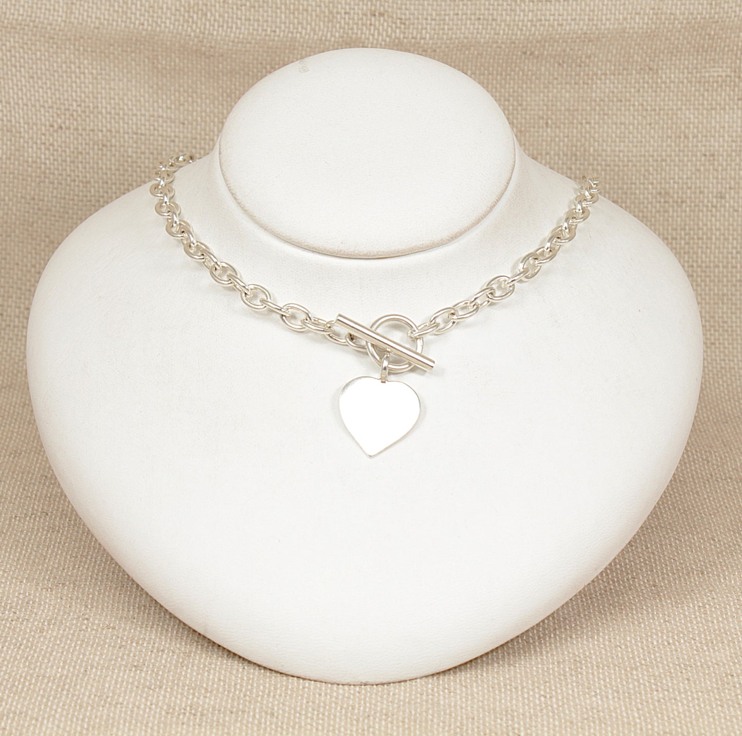 Silver necklace with a heart charm on a white stand against a beige background