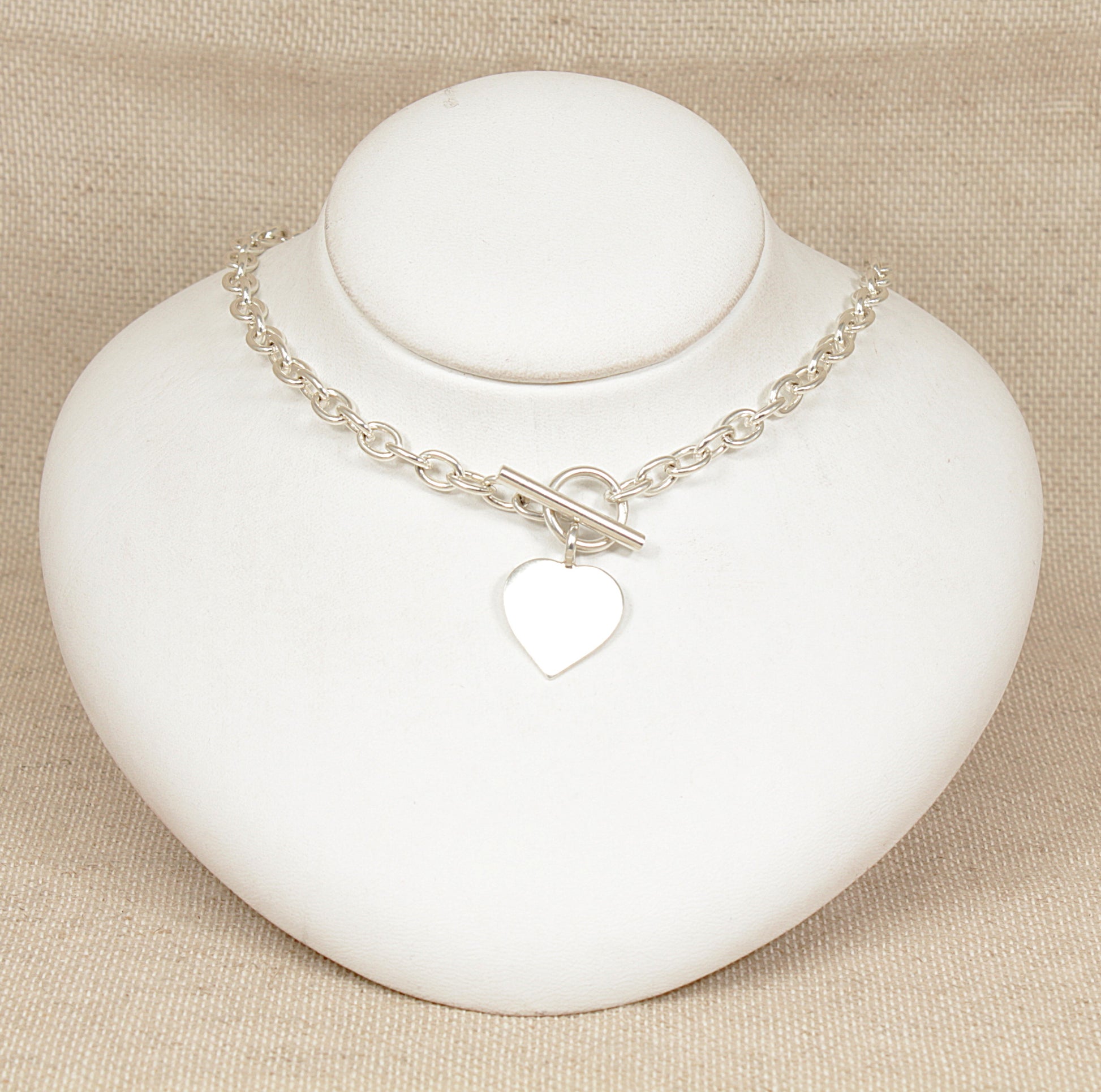 Silver necklace with a heart charm on a white stand against a beige background