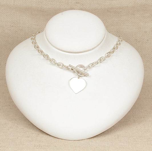 Silver necklace with a heart charm on a white stand against a beige background