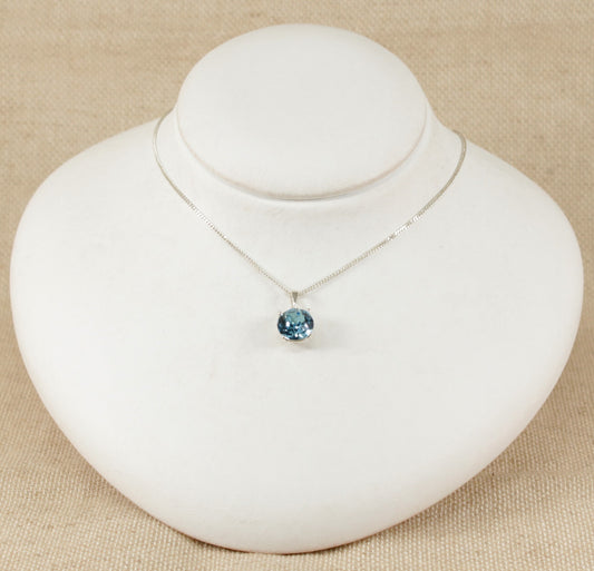 A blue crystal pendant necklace on a silver curb chain, displayed on a white mannequin.