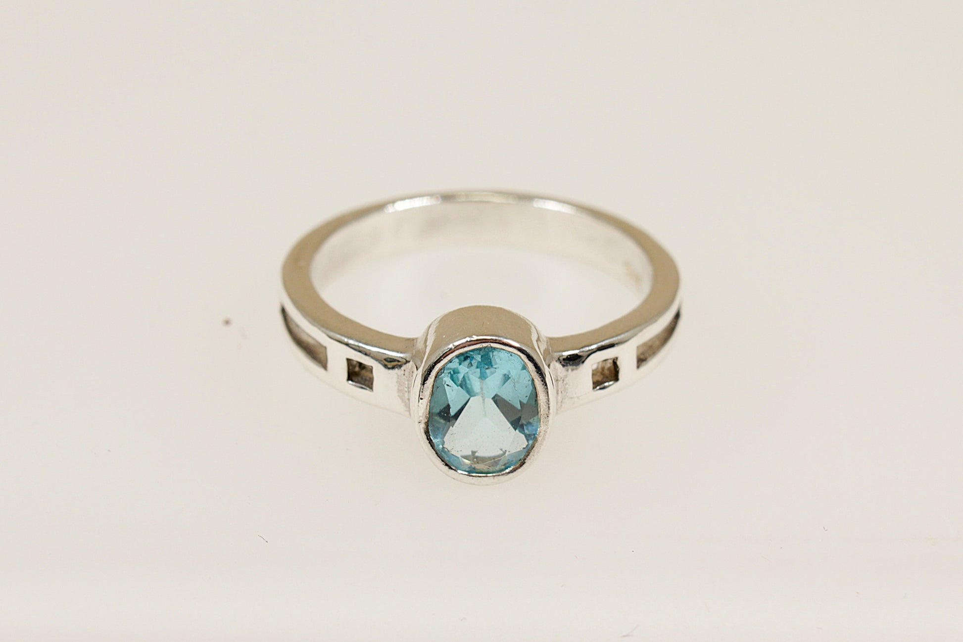 A silver ring with an oval blue faceted crystal set in a bezel, with geometric cut-outs on the shoulders.