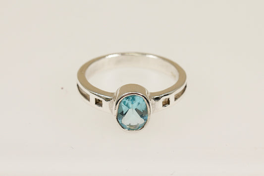 A silver ring with an oval blue faceted crystal set in a bezel, with geometric cut-outs on the shoulders.