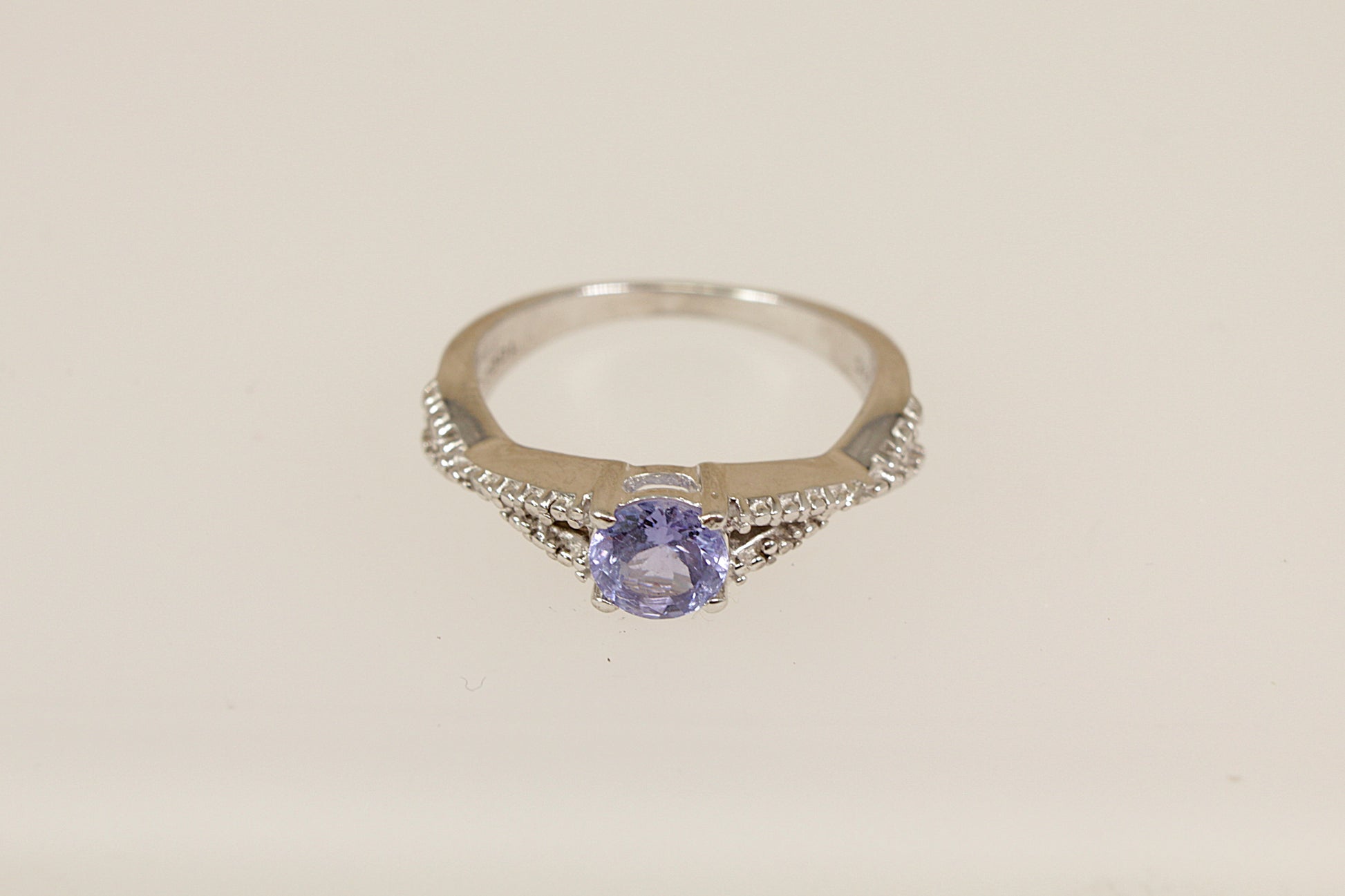 Silver ring with a purple gemstone on a light beige background