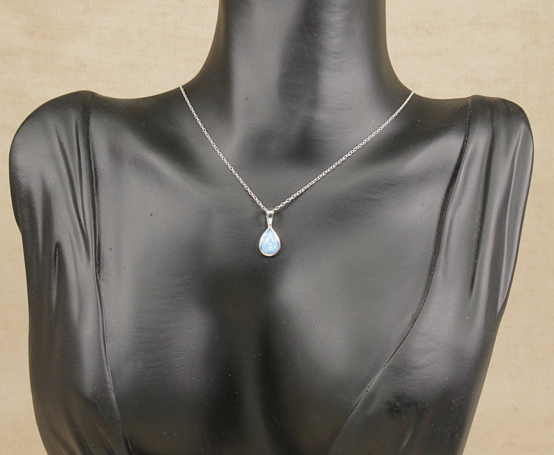 Mannequin wearing a silver necklace with a blue opal pendant on a beige background