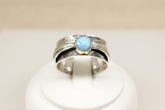 A sterling silver ring with a round blue opal gemstone in a bezel setting, featuring a nature-inspired fan or leaf design on the band.