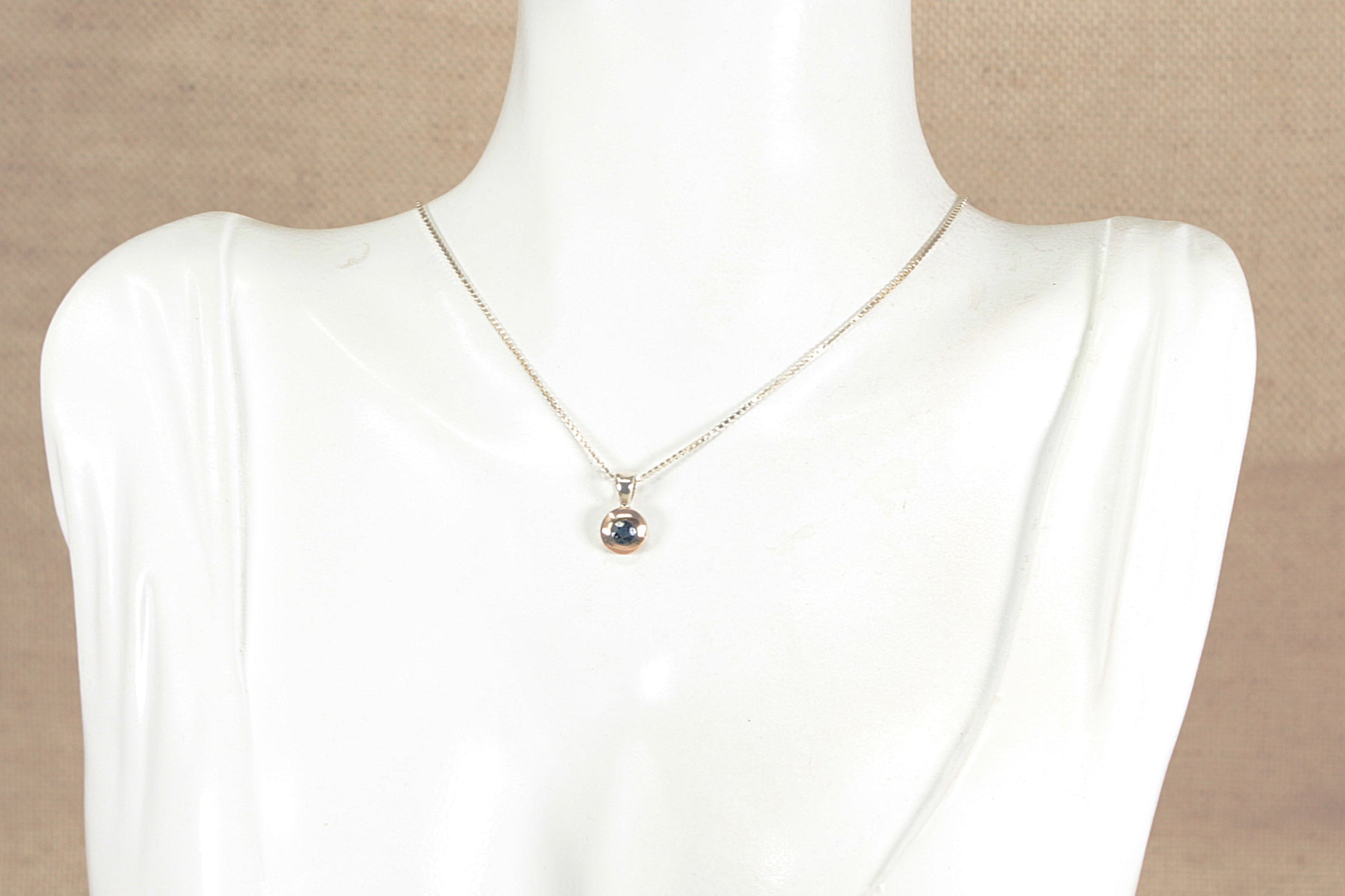 Necklace with a gold plated silver blue sapphire gemstone pendant on a mannequin against a beige background