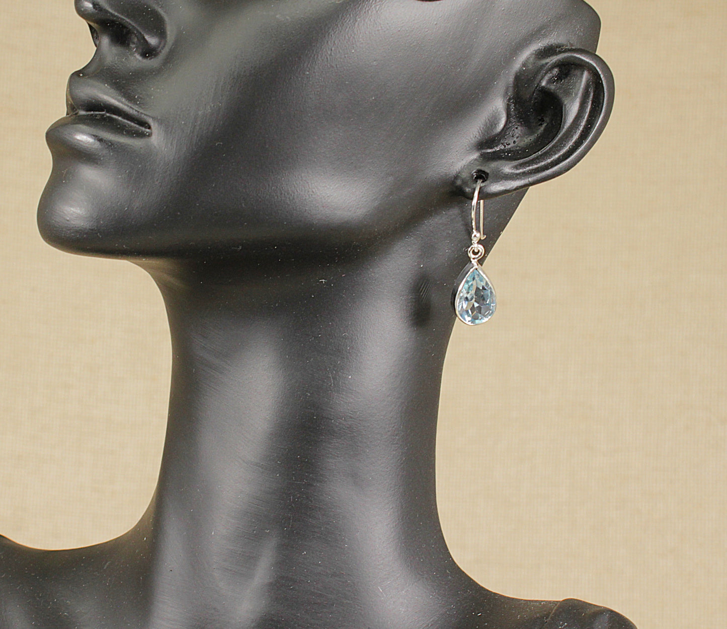 A pair of silver drop earrings with teardrop-shaped blue topaz gemstones, displayed on a mannequin head. 