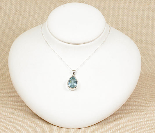 A silver teardrop pendant necklace with a blue topaz gemstone displayed on a white bust.