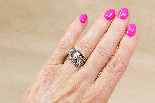 Hand with pink nail polish and a silver statement ring with blue topaz gemstones on a beige background